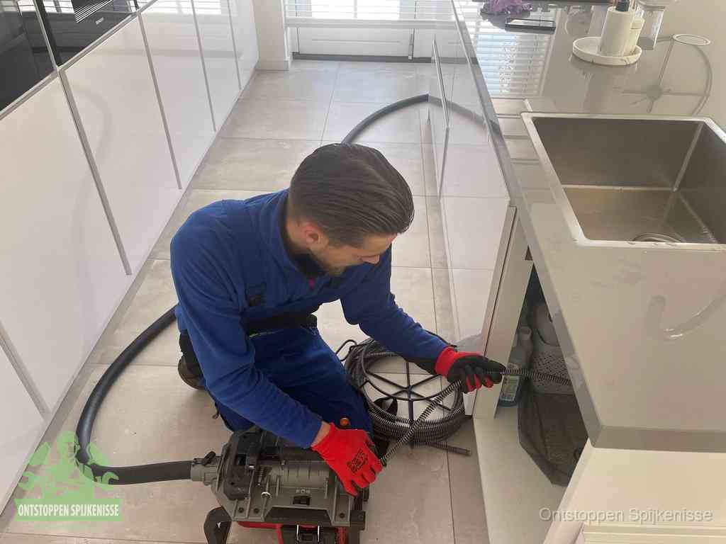 Een monteur ontstopt de keukenafvoer onder de spoelbak met een elektrische veermachine in Spijkenisse