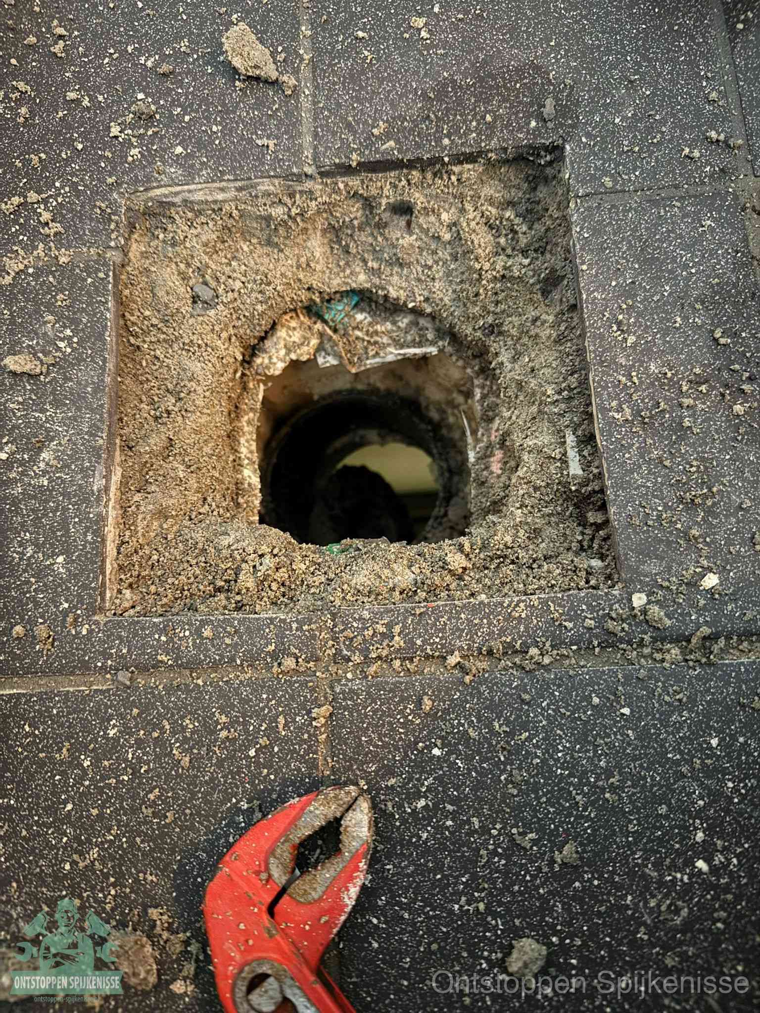 Een geopend rioolputje in een betontegelvloer met losgemaakt rooster en een zichtbare ronde afvoerbuis, het achterhalen waar de afvoerverstopping zit in Spijkenisse