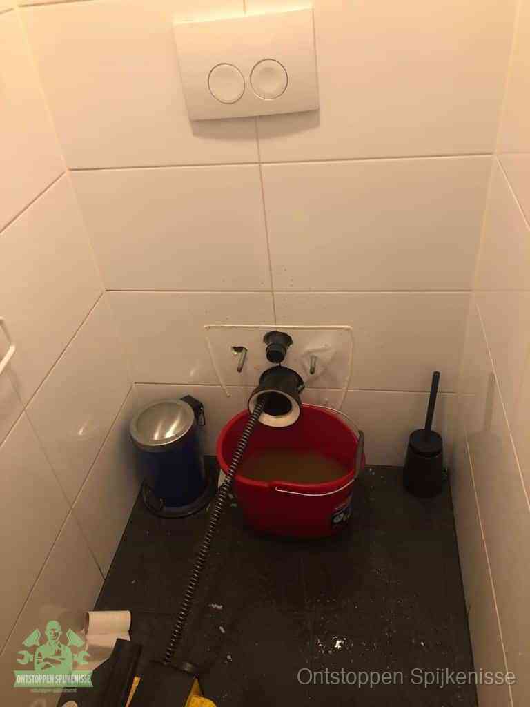 Een ontstopte wand-wc met verwijderde toiletpot waar een ontstoppingsveer in de wanduitgang verdwijnt, het achterhalen waar de verstopping zit in Spijkenisse