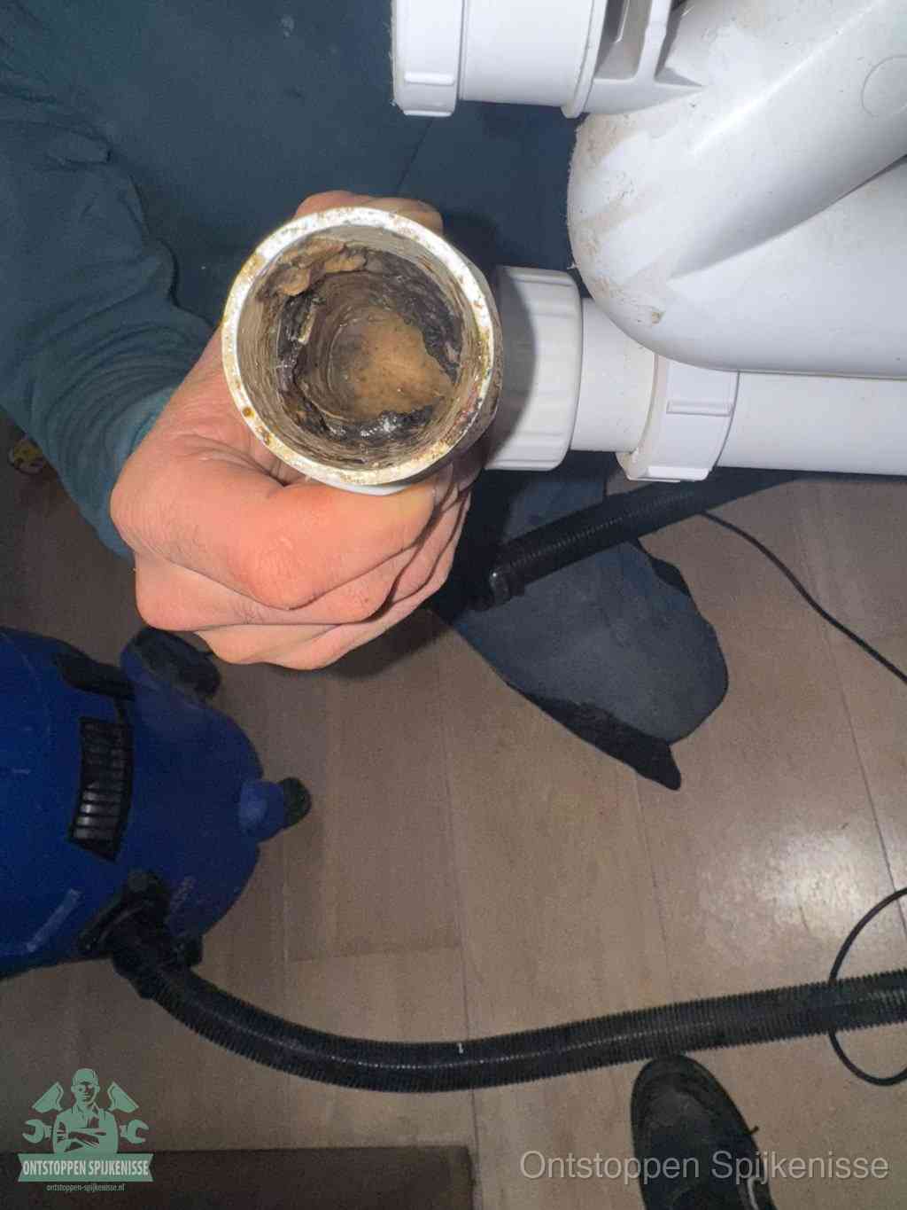 Een hand houdt een losgekoppeld PVC-afvoerbuisstuk vast dat van binnen volledig is dichtgeslibd met vet, vuil en aanslag, de meest voorkomende oorzaak van een verstopte afvoer in Spijkenisse