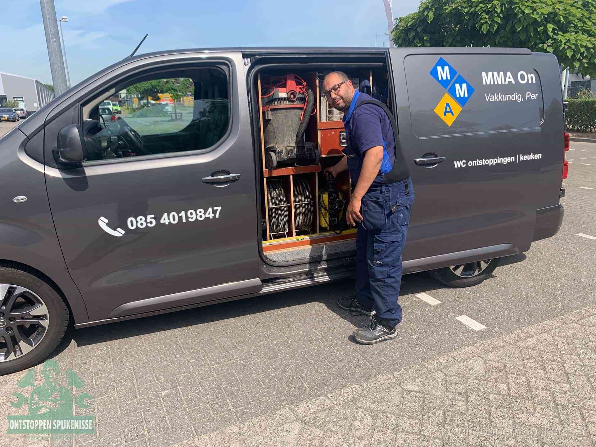 Een monteur bij de open schuifdeur van zijn bedrijfsbus op een parkeerplaats, klaar om de oorzaak van terugkerende afvoerverstoppingen aan te pakken in Spijkenisse