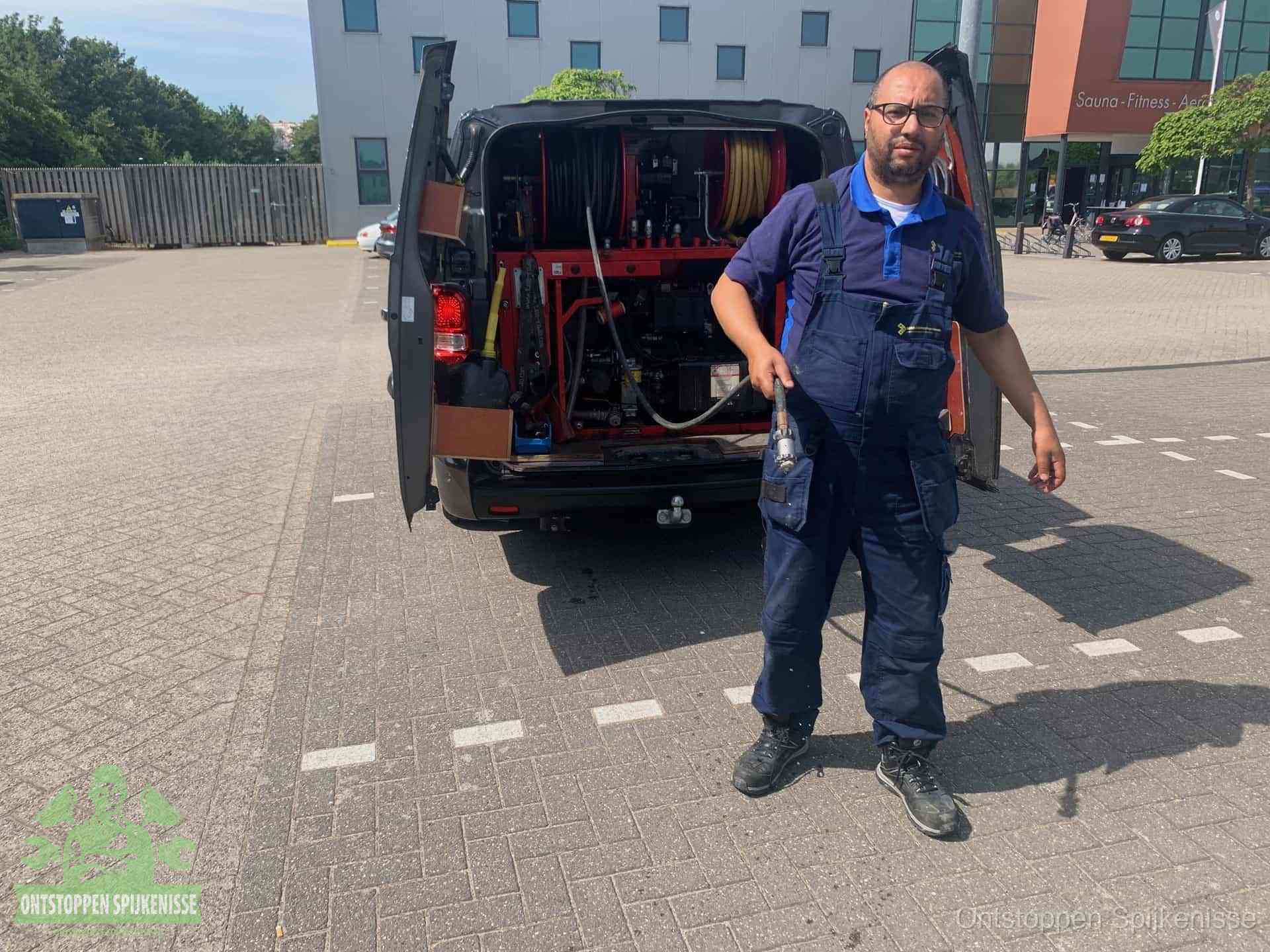 Een monteur bij zijn bestelbus met een hogedruk- en rioolreinigingsunit, klaar om de oorzaak van terugkerende wc-verstoppingen aan te pakken in Spijkenisse