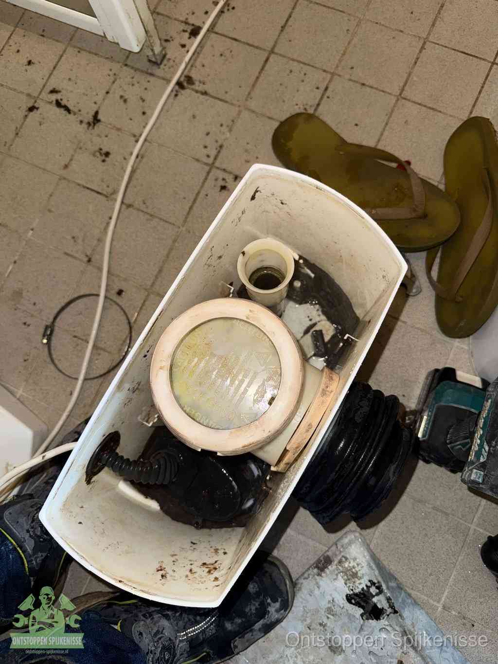 Een gedemonteerde toiletpot op de vloer met ontstoppingsveer en gereedschap ernaast, het verwijderen van een vastzittend voorwerp uit de wc in Spijkenisse