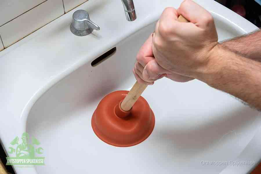 Twee handen gebruiken een rode rubberen plopper op een sanitair-afvoer om het toilet te ontstoppen in Spijkenisse