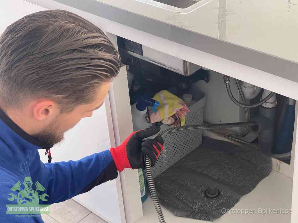 Een monteur voert een flexibele ontstoppingsveer in de afvoer om een verstopping voorbij de bocht van het toilet te bereiken in Spijkenisse
