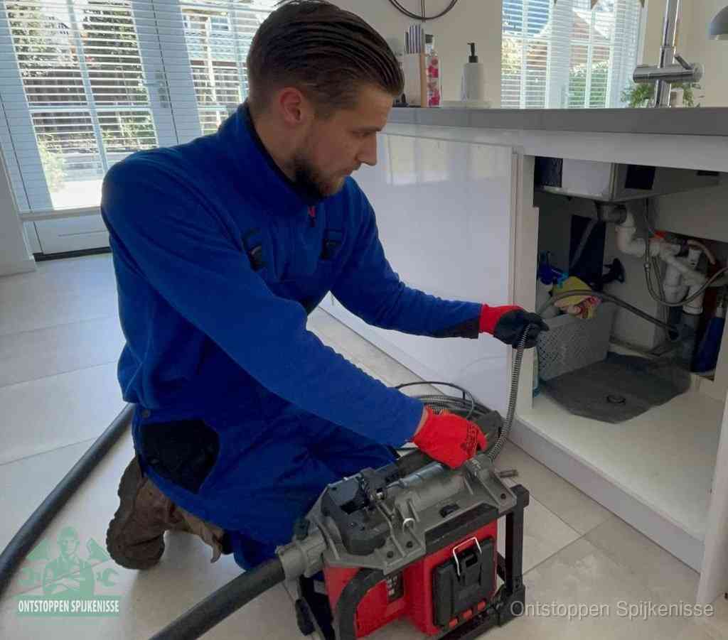 Een monteur met rode handschoenen knielt in een keuken en voert een elektrische ontstoppingsveer in tijdens het professioneel afvoer ontstoppen in Spijkenisse