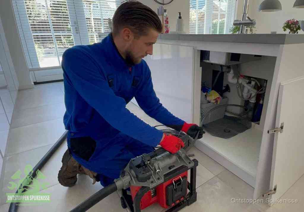 Een monteur voert een professionele elektrische ontstoppingsmachine in de afvoer onder de spoelbak tijdens het gootsteen ontstoppen in Spijkenisse